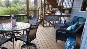 Une terrasse en bois avec une table ronde et des chaises, un canapé en osier et une lanterne décorative.