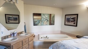 Une salle de bain moderne avec deux vasques, une grande baignoire, des meubles en bois et des œuvres d’art accrochées aux murs.