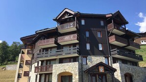 Un hotel a più piani con balconi, facciata in pietra e ambientazione in una località sciistica.