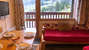 Una stanza accogliente con un tavolo da pranzo in legno apparecchiato per due persone, un divano rosso con una coperta e un televisore montato a parete.