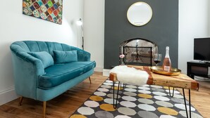 A modern living room with a teal sofa, a round mirror, a fireplace, and a television. - Cosy Home Near Station, Parking, Netflix, Sleeps 5 (Coventry)