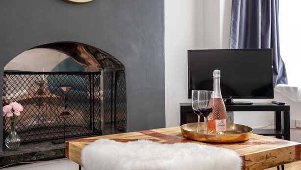 A modern living room with a fireplace, a television, and a wooden table with a bottle of wine and a glass. - Cosy Home Near Station, Parking, Netflix, Sleeps 5 (Coventry)
