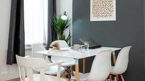 A modern dining area with a white table, four white chairs, a laptop, a plant, and a framed artwork on the wall. - Cosy Home Near Station, Parking, Netflix, Sleeps 5 (Coventry)