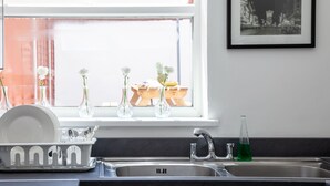 A kitchen with a sink, a dish rack, and three vases with flowers on the windowsill. - Cosy Home Near Station, Parking, Netflix, Sleeps 5 (Coventry)