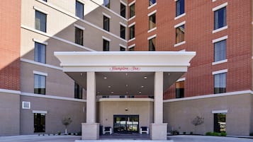 Entrada de hotel con zona cubierta, varias ventanas y un letrero que dice 'Hampton Inn'.