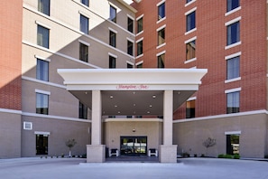 Entrada de hotel con zona cubierta, varias ventanas y un letrero que dice 'Hampton Inn'.