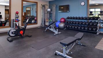A gym with exercise equipment, a bench, and a wall-mounted dumbbell rack.