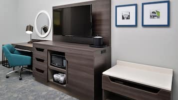Une chambre d’hôtel équipée d’un téléviseur à écran plat, d’un bureau avec une chaise, d’un banc, d’un four à micro-ondes et d’un petit réfrigérateur. Deux tableaux encadrés ornent le mur.