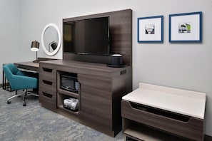 Habitación de hotel con televisión de pantalla plana, escritorio con silla, banca, microondas y refrigerador pequeño. Hay dos cuadros en la pared.
