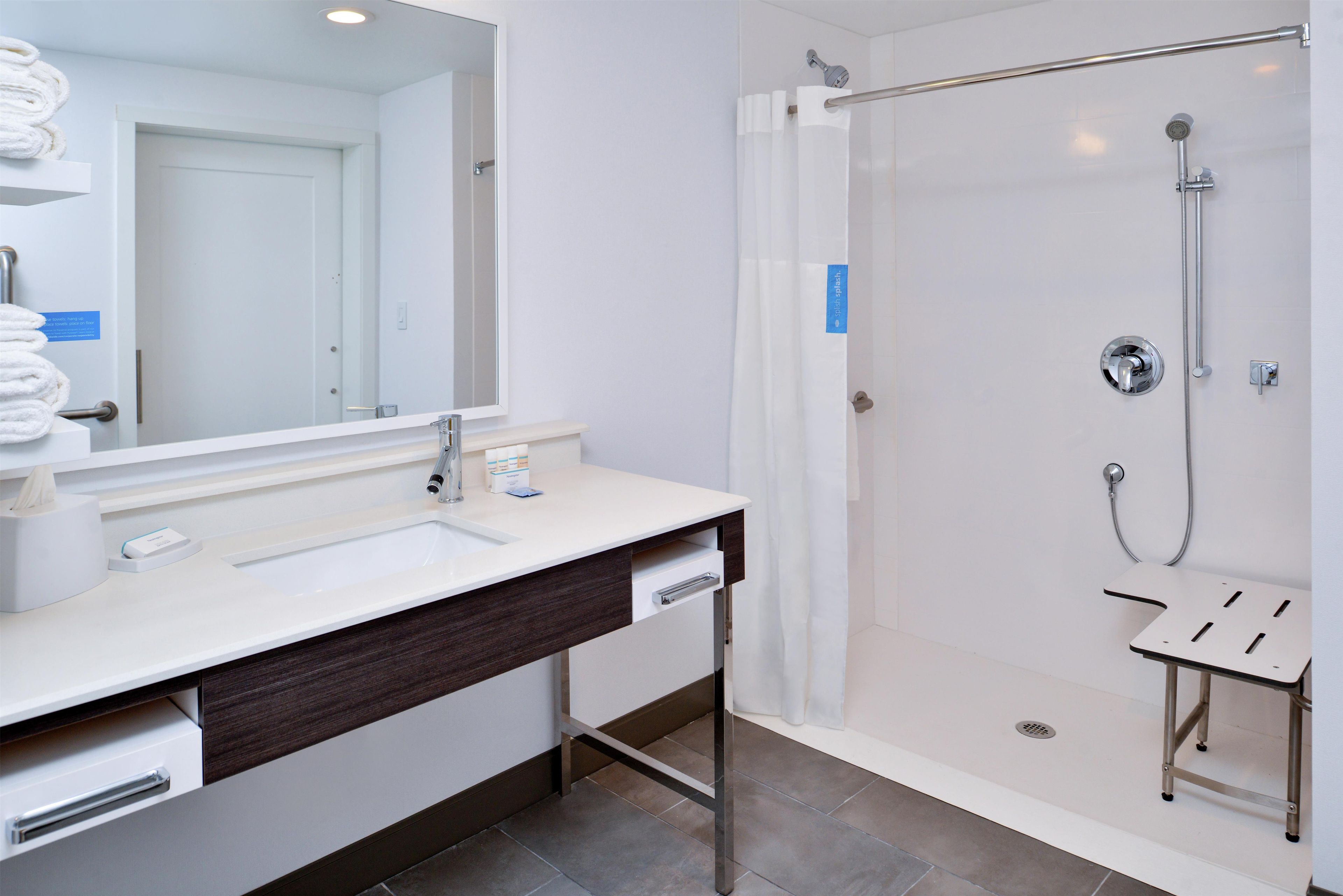A modern bathroom with a large mirror, a sink, a shower with a glass door, and a small stool.