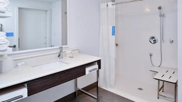 A modern bathroom with a large mirror, a sink, a shower with a glass door, and a small stool.