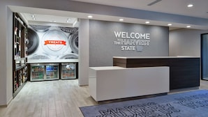 A modern reception area with a 'Welcome to the Harvest State' sign, a refrigerated display case, and a reception desk. - Hampton Inn Cedar Falls Downtown (Cedar Falls)
