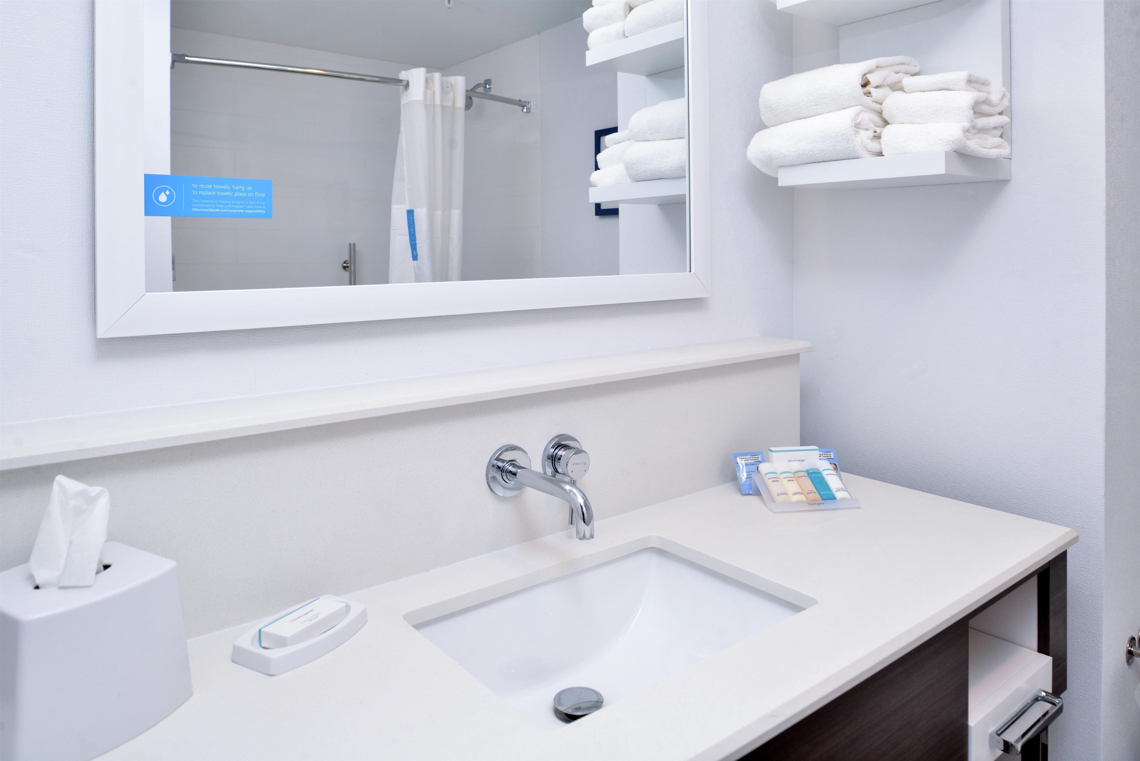 Un baño con un lavabo blanco, un espejo y un perchero con toallas dobladas.