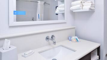 Un baño con un lavabo blanco, un espejo y un perchero con toallas dobladas.