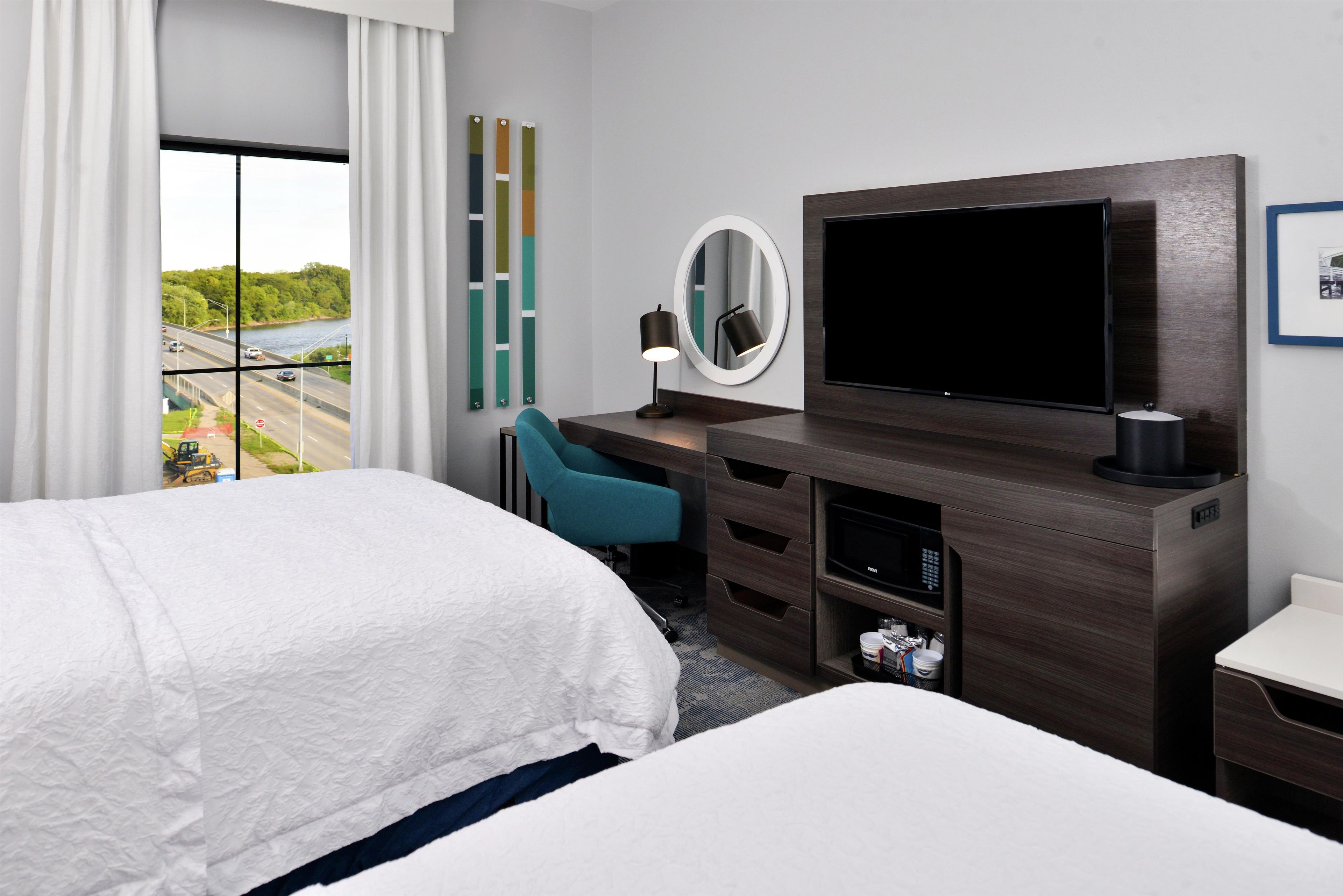 A hotel room with a large bed, a desk with a chair, a television, and a view of a highway.