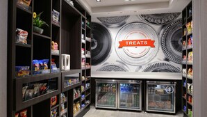 A store with shelves stocked with snacks and drinks, and a wall with a 'Treats' sign. - Hampton Inn Cedar Falls Downtown (Cedar Falls)