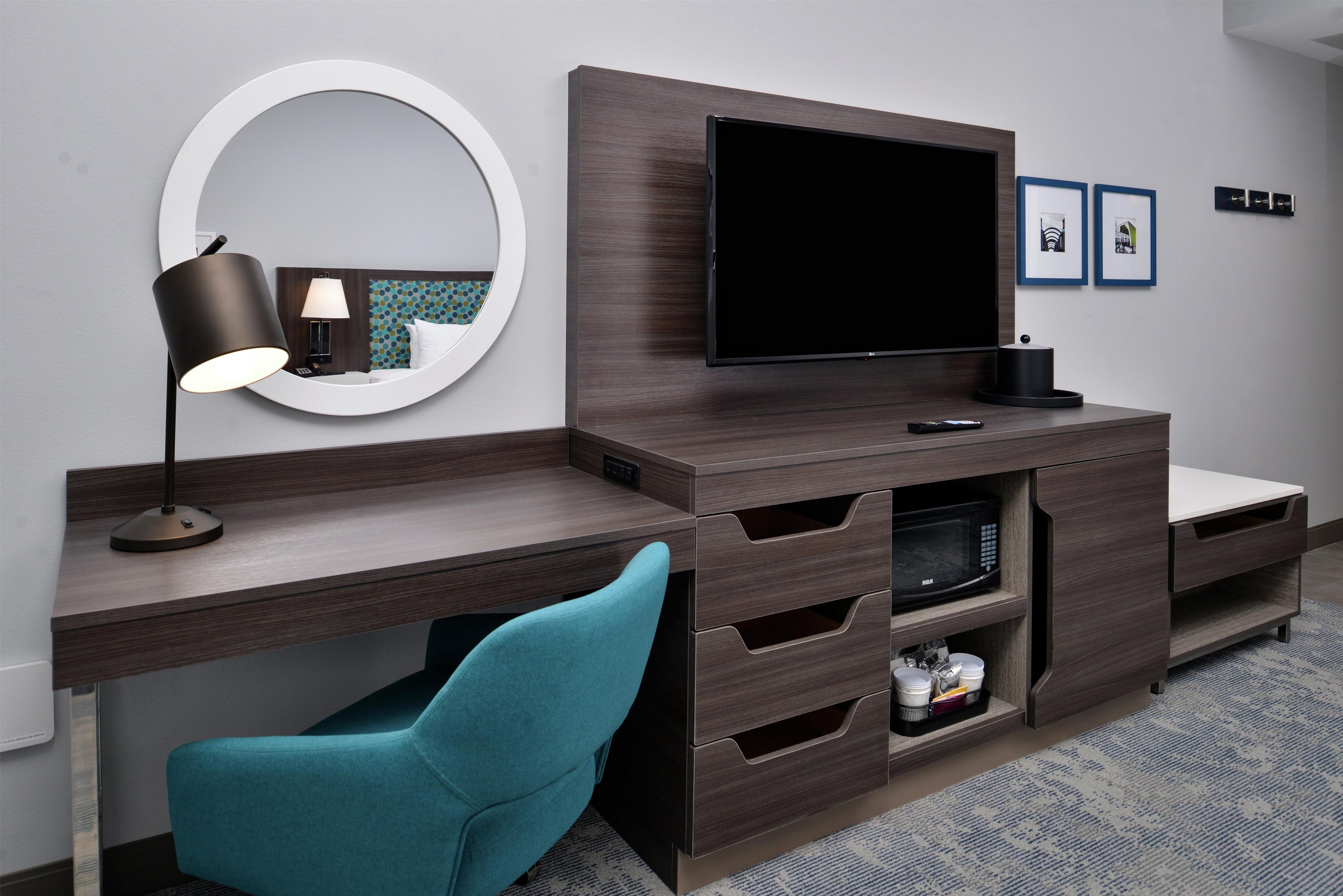 A modern hotel room with a flat-screen TV, a desk with a lamp, a chair, and a microwave.