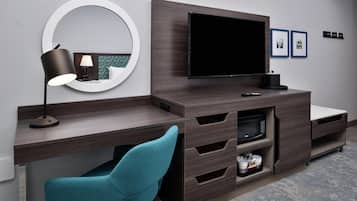 A modern hotel room with a flat-screen TV, a desk with a lamp, a chair, and a microwave.