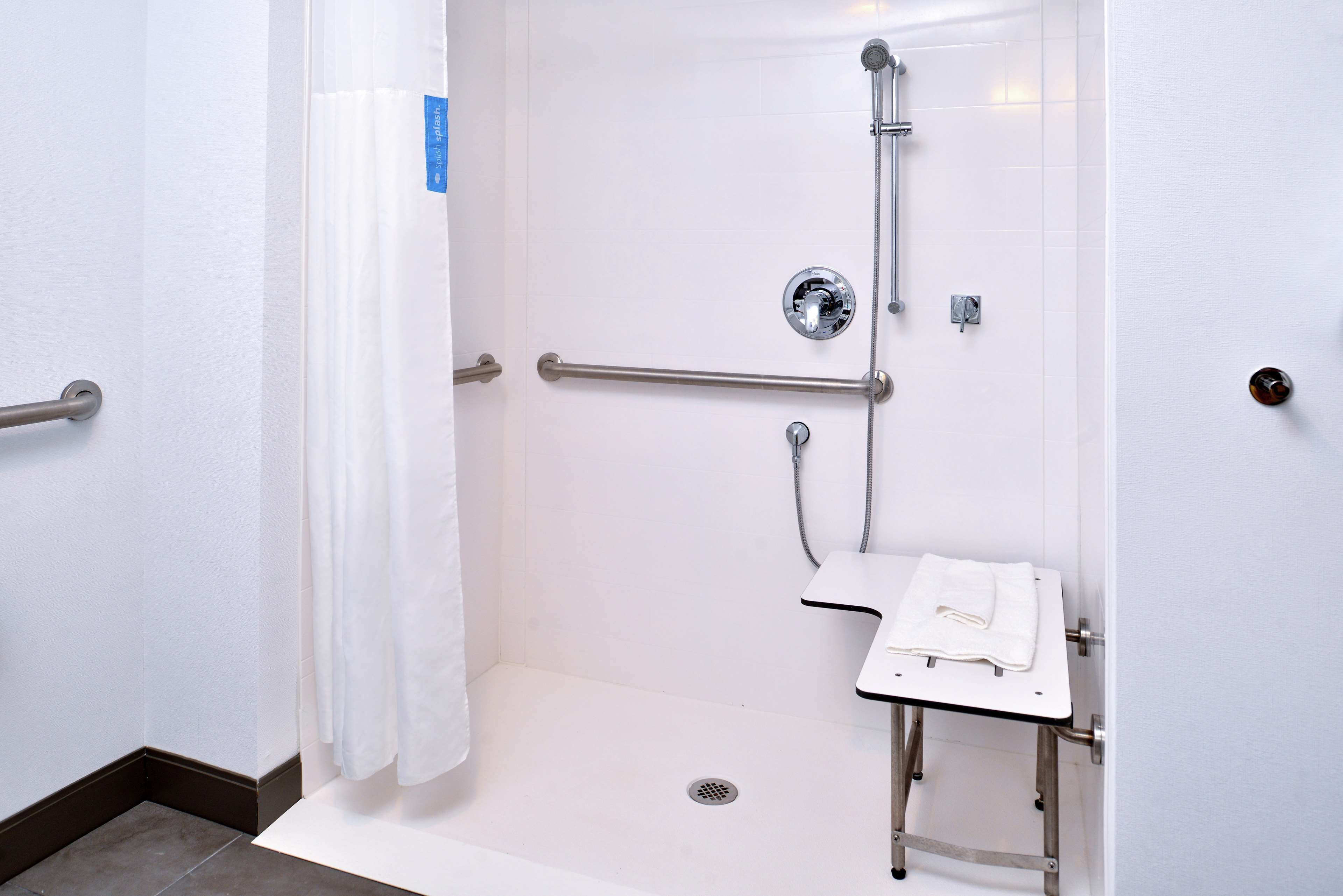 A handicap-accessible shower with grab bars, a white sink, and a towel rack.