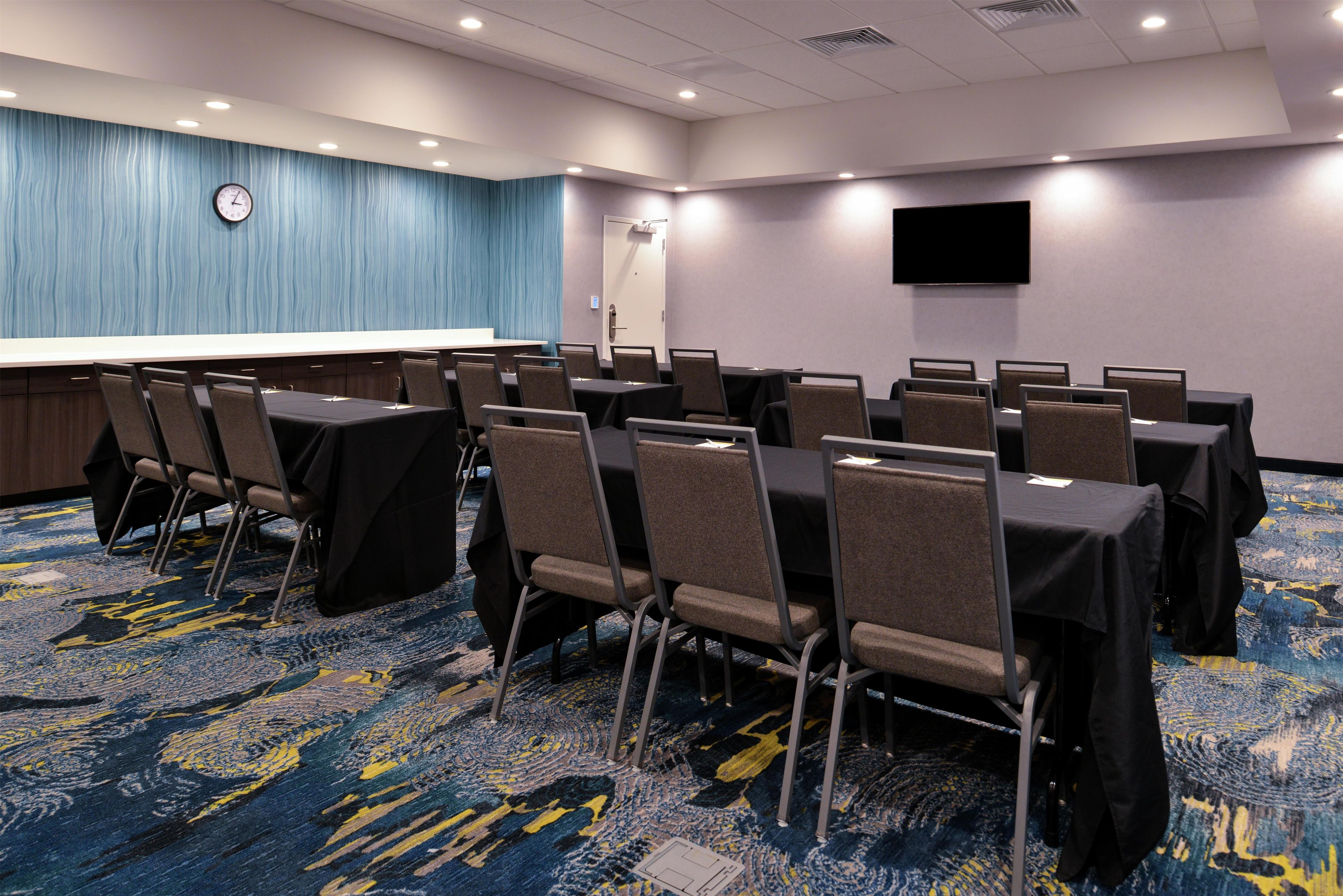 A conference room with tables and chairs, a clock on the wall, and a flat-screen TV.