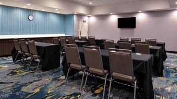 A conference room with tables and chairs, a clock on the wall, and a flat-screen TV.