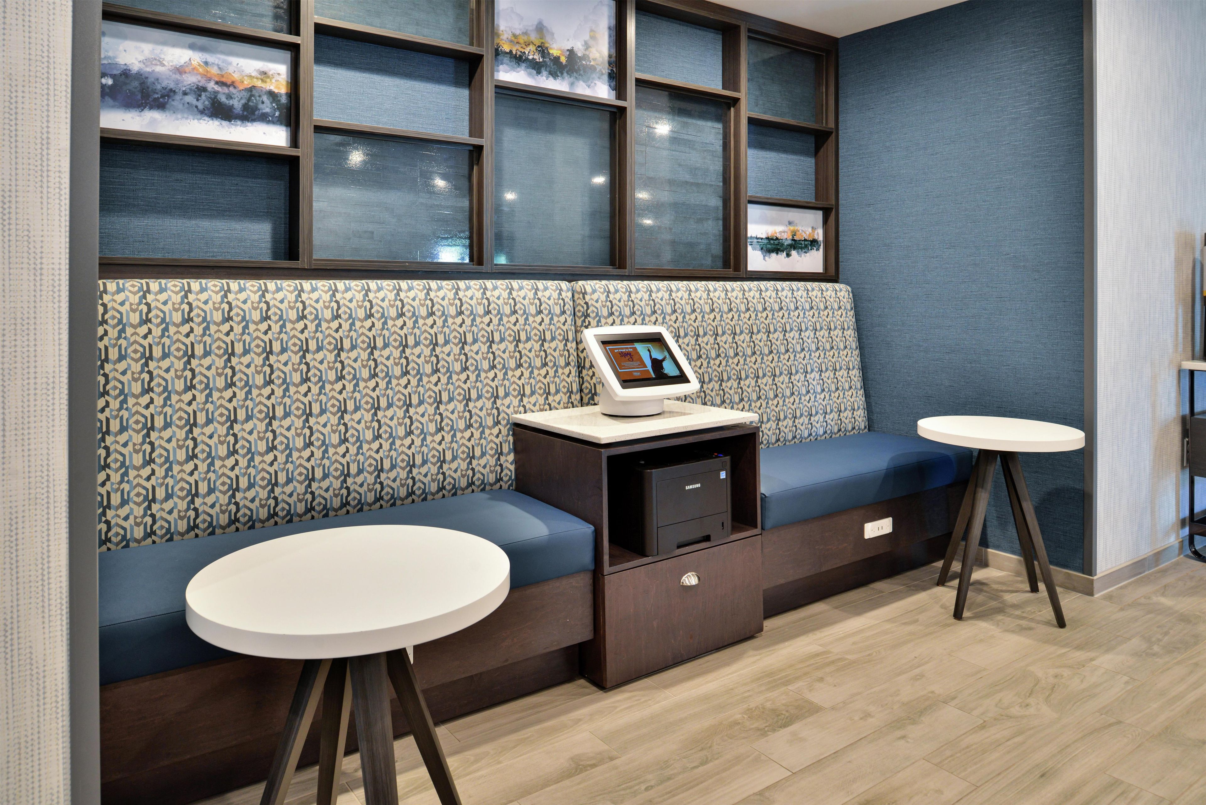 Un coin salon comprenant un canapé, deux petites tables, un appareil Samsung et un revêtement mural à motifs.