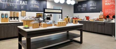 Une cuisine moderne dotée d’un îlot central, de divers appareils de cuisine et d’un panneau indiquant que le service du petit-déjeuner est assuré.