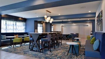 A modern hotel lobby with a bar area, seating arrangements, and a patterned carpet.