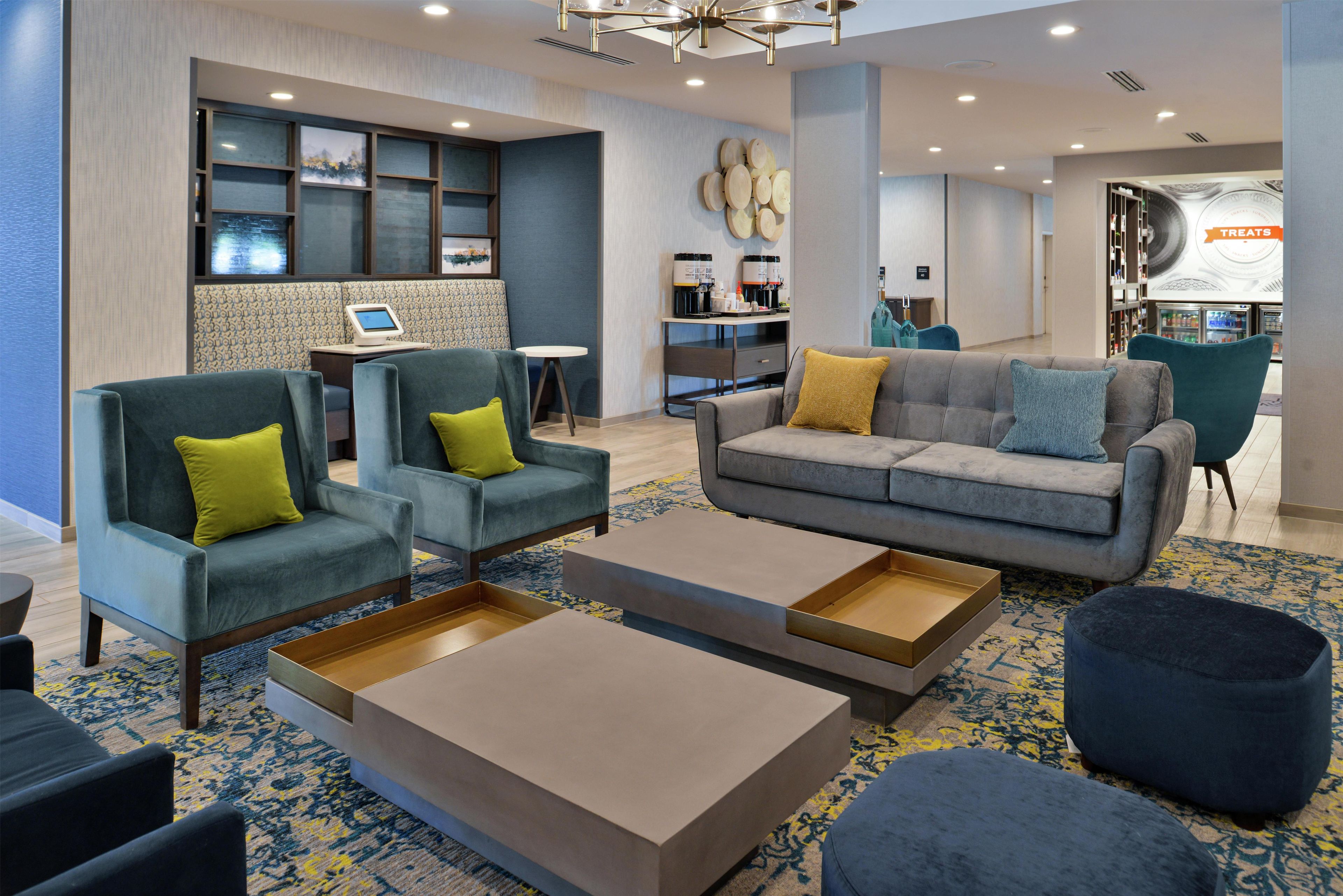 A modern hotel lobby with seating areas, a coffee station, and a visible counter.