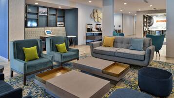 A modern hotel lobby with seating areas, a coffee station, and a visible counter.