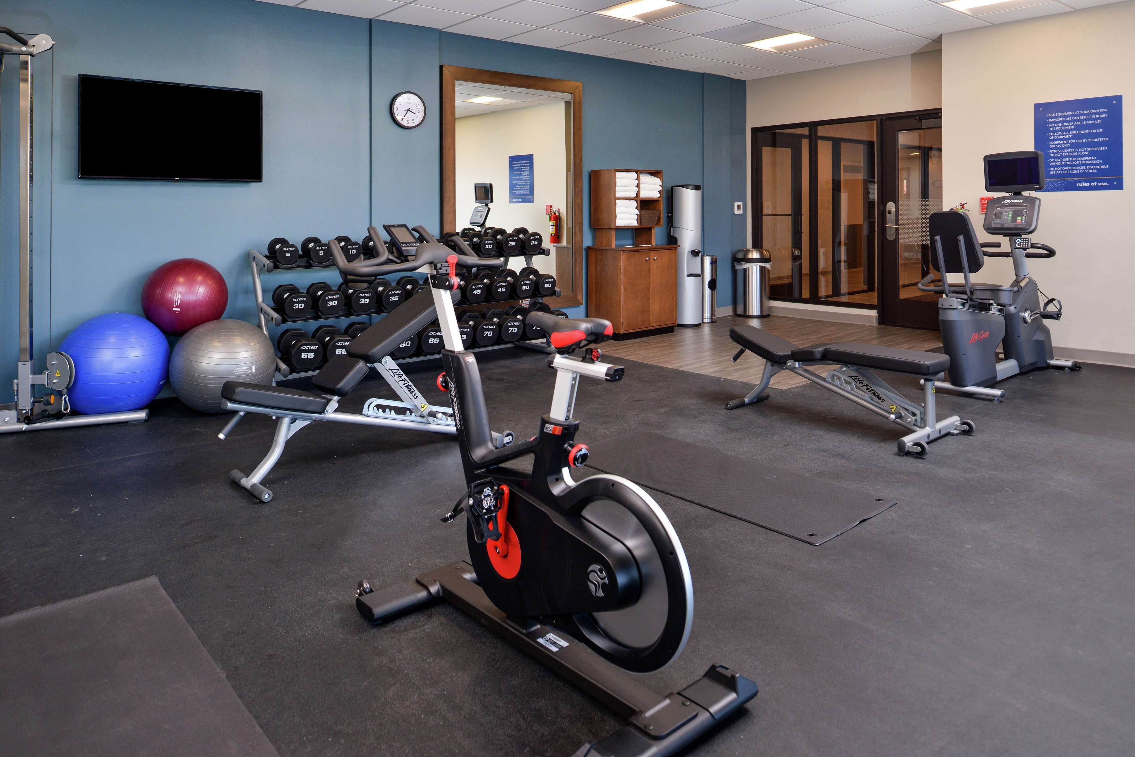 A gym with exercise equipment, a television, and a clock on the wall.