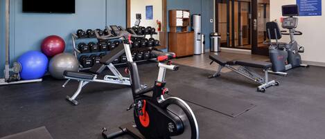 A gym with exercise equipment, a television, and a clock on the wall.