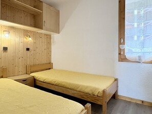 A room with two beds, wooden walls, a window with a view, and a wooden cabinet. - Cristallin 34 - Charming 2-room apartment (LES AVANCHERS VALMOREL)