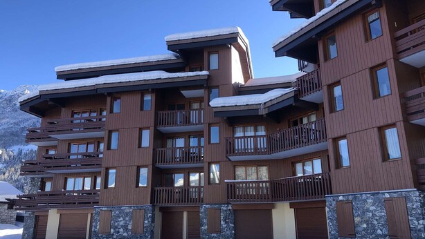 Ein mehrstöckiges Hotel mit Balkonen, Steinverzierungen und einem verschneiten Berg im Hintergrund.