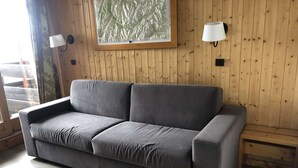 Ein graues Sofa in einem Raum mit Holzwänden, einem gerahmten Bild und zwei Wandlampen.
