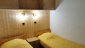 Eine kleine, einfache Unterkunft mit zwei Holzbett und einem Holzschrank, sowie zwei Wandleuchten.