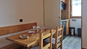 Ein Holzespeisesaal mit Stühlen, einer Schüssel und Weingläsern. Im Hintergrund ist eine Küche mit Holzausbau und einem Fenster zu sehen.