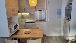 A compact kitchen with a wooden table, chairs, a sink, a dishwasher, and a refrigerator.