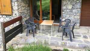 An outdoor patio with a stone wall, a wooden bench, and a table with four chairs.