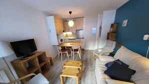 A compact living space with a sofa, a TV, a dining table with chairs, and a kitchenette.