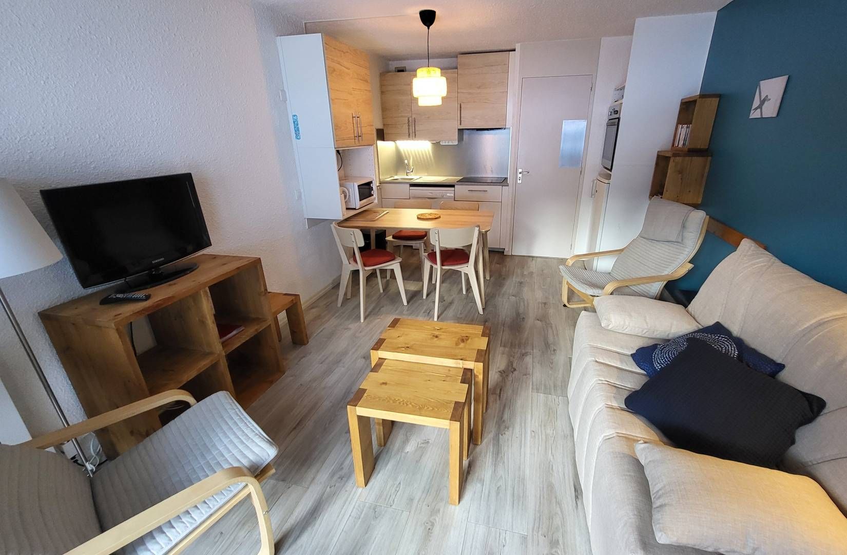 En kompakt opholdsstue med fjernsyn, træmøbler, sofa og et tekøkken.