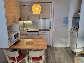 A compact kitchen with a dining table, chairs, a hanging light fixture, and built-in appliances. - Le Cheval Noir 9 - Cosy renovated 2-room apartment with balcony (LES AVANCHERS VALMOREL)