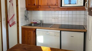 A compact kitchen with wooden cabinets, a built-in microwave, a dishwasher, and a wooden countertop.