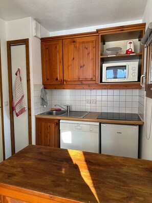 A compact kitchen with wooden cabinets, a built-in microwave, a dishwasher, and a wooden countertop.
