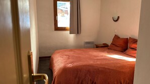 A bedroom with a large bed, a window with curtains, a bedside table, and a wall-mounted light fixture.