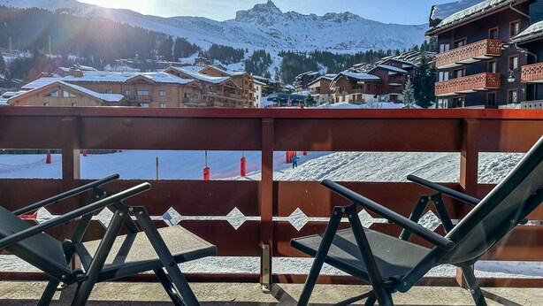 A balcony with metal chairs, overlooking a snowy mountain landscape with buildings.