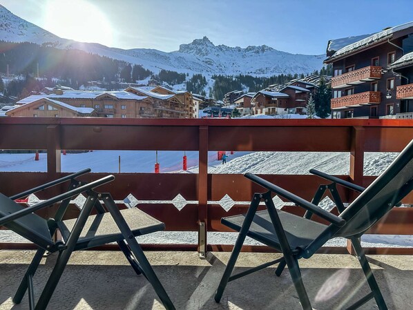 Un balcón con sillas de metal, con vista a un paisaje montañoso nevado y edificios.