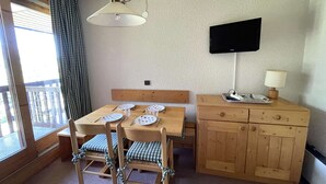 Ein Essbereich mit Holztisch und Stühlen, einem an der Wand montierten Fernseher und einem Fenster mit Vorhängen.