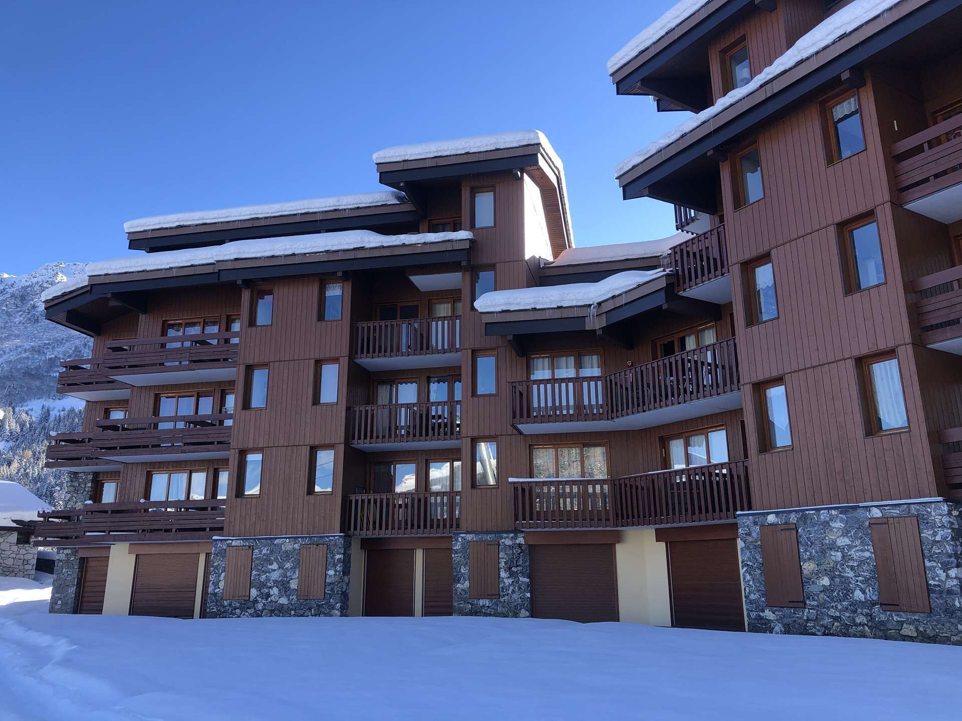Un hôtel à plusieurs étages, doté de balcons, d’éléments décoratifs en pierre et surplombant un paysage montagneux enneigé.
