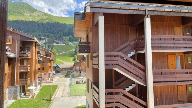 Ein mehrstöckiges Holzgebäude mit Balkonen und Blick auf ein grünes Tal und Berge.